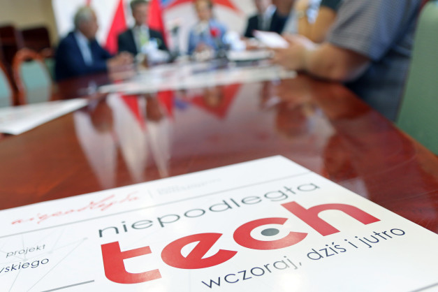 Na stole leży materiał z napisem "niepodległa tech". W tle widać ludzi siedzących przy stole.