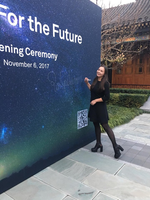Kobieta w czarnej sukience podpisuje się na tle baneru "For the Future". Tło przedstawia nocne niebo.