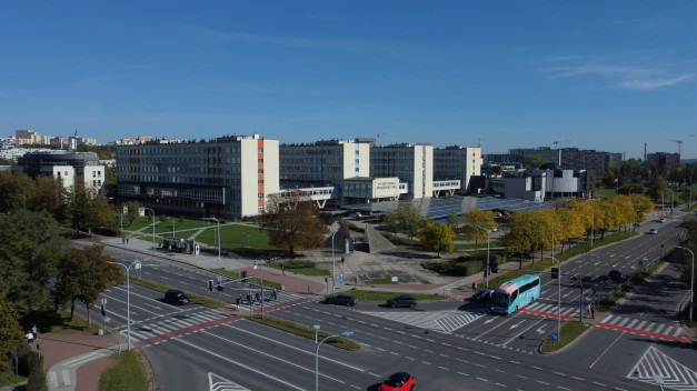 Budynek Politechniki Świętokrzyskiej, droga z samochodami i autobusem, drzewa. Kontekst: kampus uniwersytecki, miasto.