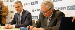 Dwóch mężczyzn w garniturach podpisuje dokumenty. W tle widoczne logo HSW PGZ.
