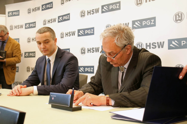 Dwóch mężczyzn w garniturach podpisuje dokumenty. W tle widoczne logo HSW PGZ.