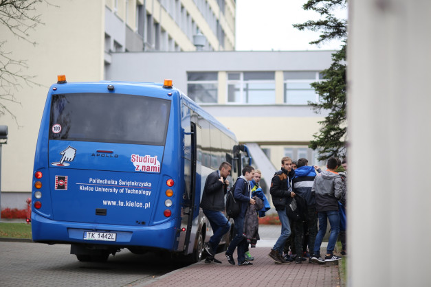Niebieski autobus z napisem "Politechnika Świętokrzyska" i grupą młodych ludzi. Kontekst: wycieczka lub transport studencki.