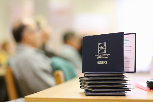 Stos indeksów Politechniki Świętokrzyskiej na stole. W tle niewyraźne sylwetki ludzi.