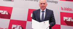 Mężczyzna w garniturze trzyma dokument. W tle logo Politechniki Świętokrzyskiej.