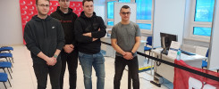 Czterech młodych mężczyzn stoi w pomieszczeniu z banerem "WorldSkills Poland". W tle widać biurka z komputerami i okna.