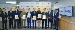 Grupa osób w garniturach i mundurze odbiera dyplomy. W tle logo NASK i Huawei.