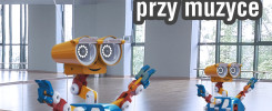 Dwa roboty-zabawki w sali gimnastycznej. Jeden robot jest w pełni widoczny, drugi odbija się w lustrze.