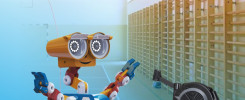 Kolorowy robot i wioślarski trenażer stoją na hali sportowej. Kontekst: Politechnika Świętokrzyska, sekcja wioślarska.