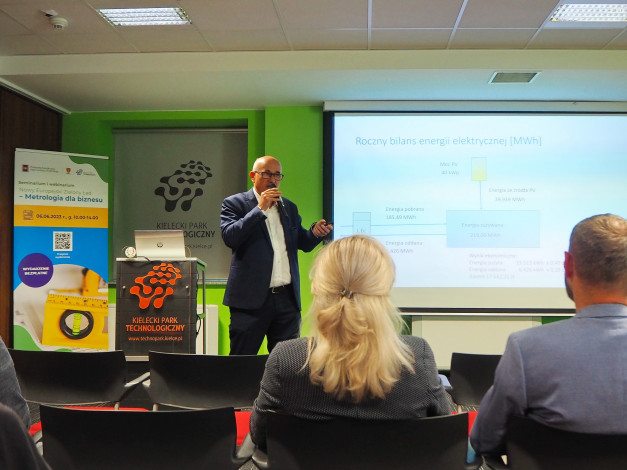 Mężczyzna przemawia na seminarium. Na ekranie widoczny jest wykres "Roczny bilans energii elektrycznej".