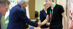 Dwóch mężczyzn się wita. Jeden w garniturze, drugi w czarnej koszulce z medalem. Kontekst: ceremonia wręczenia nagród.