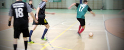Piłkarze w halach sportowych podczas meczu. Kluczowe obiekty: piłka, zawodnicy w koszulkach z numerami 18 i 17.