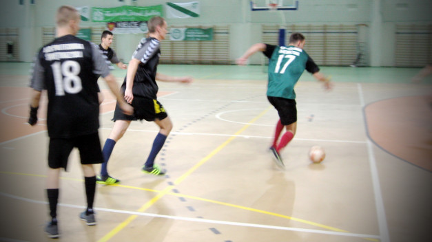 Piłkarze w halach sportowych podczas meczu. Kluczowe obiekty: piłka, zawodnicy w koszulkach z numerami 18 i 17.