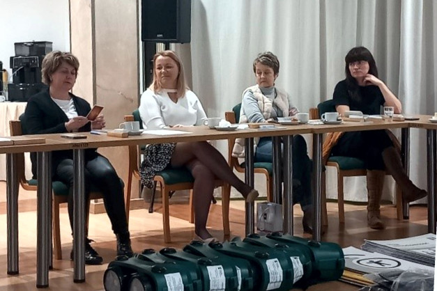 Cztery kobiety siedzą przy stole podczas spotkania. Na stole są kubki i dokumenty.