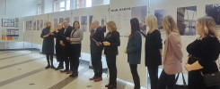Grupa osób stoi przed wystawą prac architektonicznych. Wystawa zawiera plakaty z podpisami, m.in. "Miasto Dostępne".