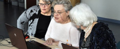 Trzy kobiety z siwymi włosami patrzą na laptopy. Kobiety siedzą przy stole.