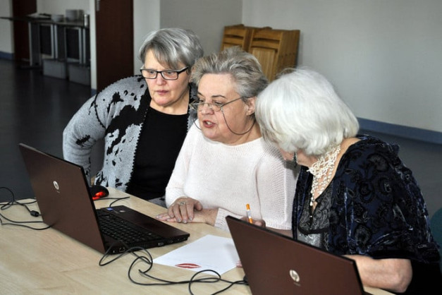 Trzy kobiety z siwymi włosami patrzą na laptopy. Kobiety siedzą przy stole.